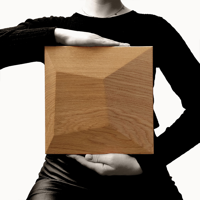 PILLOW OAK IN HAND PYRAMID OAK Holzpaneel von Dekostyl, gehalten von einer Hand, zeigt die pyramidenförmige Struktur und natürliche Holzmaserung.